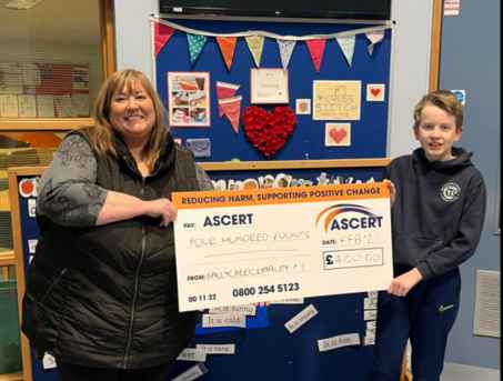 Fiona, ASCERT's Fundraising and Marketing Manager stands with a young boy from Ballymacash Primary School. They are both holding either side of a large cheque with £400 written on it, donated by the school to ASCERT.