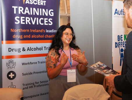 Elena, our Training Officer speaking to z man in a suit. She is wearing a pink tank top and had a black and red flower tattoo on her right arm.