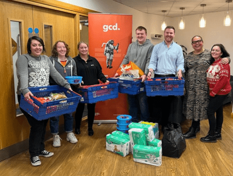 ASCERT Staff collect donated Christmas Hamper supplies. Four people are holding blue containers of different items.  