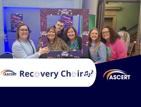 Six members of ASCERT's recovery choir stand smiling for a photo holding a BBC Sing photo frame.  